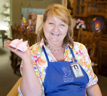 Maria D’Elia holds up a tiny pair of baby booties that she custom makes and donates for sale to the Hospice of the Valley White Dove Thrift Shoppe at 5035 N. 7th Ave., where she also volunteers (photo by Jaime Scowley, HOV).