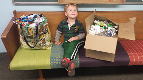 Caleb Camp, 3, a student at Cross Roads Preschool and Kindergarten, shows off some of his family’s recyclables that are being brought in to the new recycling collection bins at the school (photo courtesy of Melisa Camp).