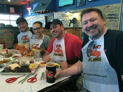 Owners Dan Sevilla, his wife Autum Perry-Sevilla and Andrew Diamond, along with Derek Still, general manager of The Angry Crab Shack, prepare to dive into a plethora of seafood and barbecue. The bibs are part of the dress code at the restaurant (photo by Patty Talahongva).